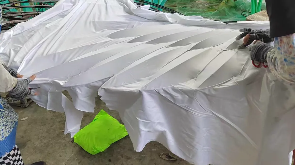 Dos personas tensando a mano un paño de seda blanca sobre el armazón del ala de una figura