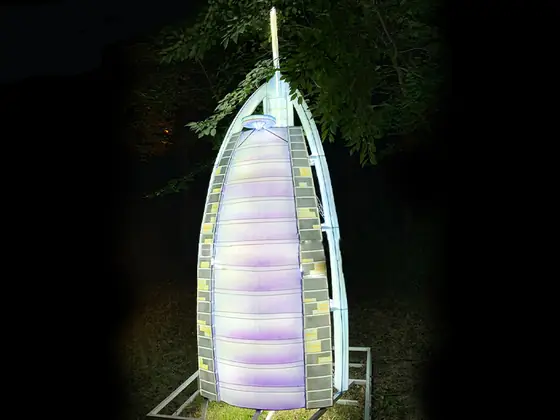 Réplica luminosa LED del hotel Burj Al Arab con su silueta de vela, iluminada en blanco, violeta y verde sobre césped