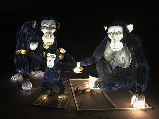 Familia de chimpancés luminosos LED: dos adultos de pelaje oscuro y una cría en el centro, con caras y pecho iluminados en tono claro