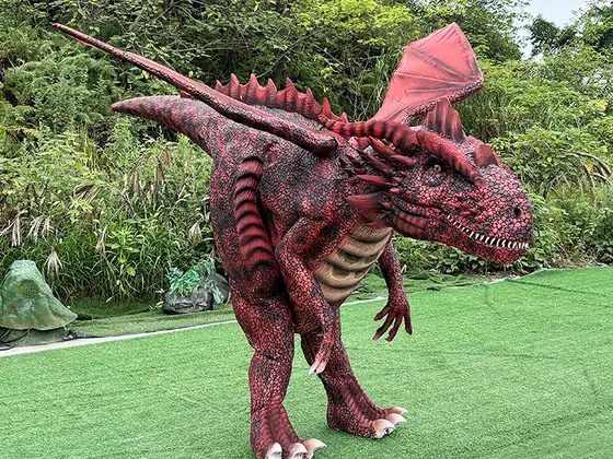 Disfraz caminante de dragón rojo con escamas marcadas, alas membranosas plegadas sobre el lomo y cuernos en la cabeza, sobre césped