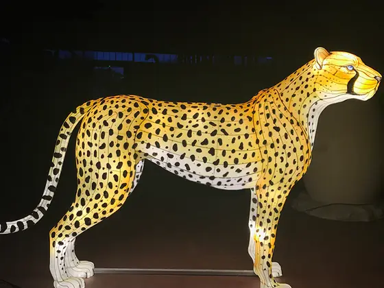 Guepardo luminoso LED a tamaño real, de perfil, con el pelaje amarillo iluminado y las manchas negras marcadas, sobre peana metálica