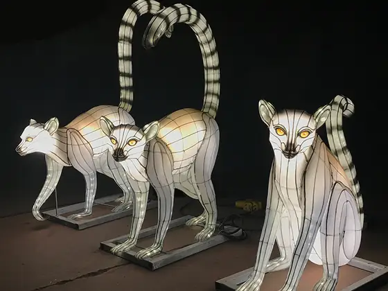 Tres lémures de cola anillada luminosos LED sobre fondo oscuro, dos erguidos y uno sentado, con la cola a rayas levantada en arco