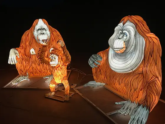 Dos orangutanes luminosos LED con el pelo largo anaranjado iluminado y la cara clara; uno lleva una cría agarrada al pecho