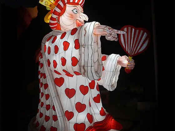 Figura luminosa de la reina de corazones con corona, vestido blanco cubierto de corazones rojos y un abanico a rayas en la mano
