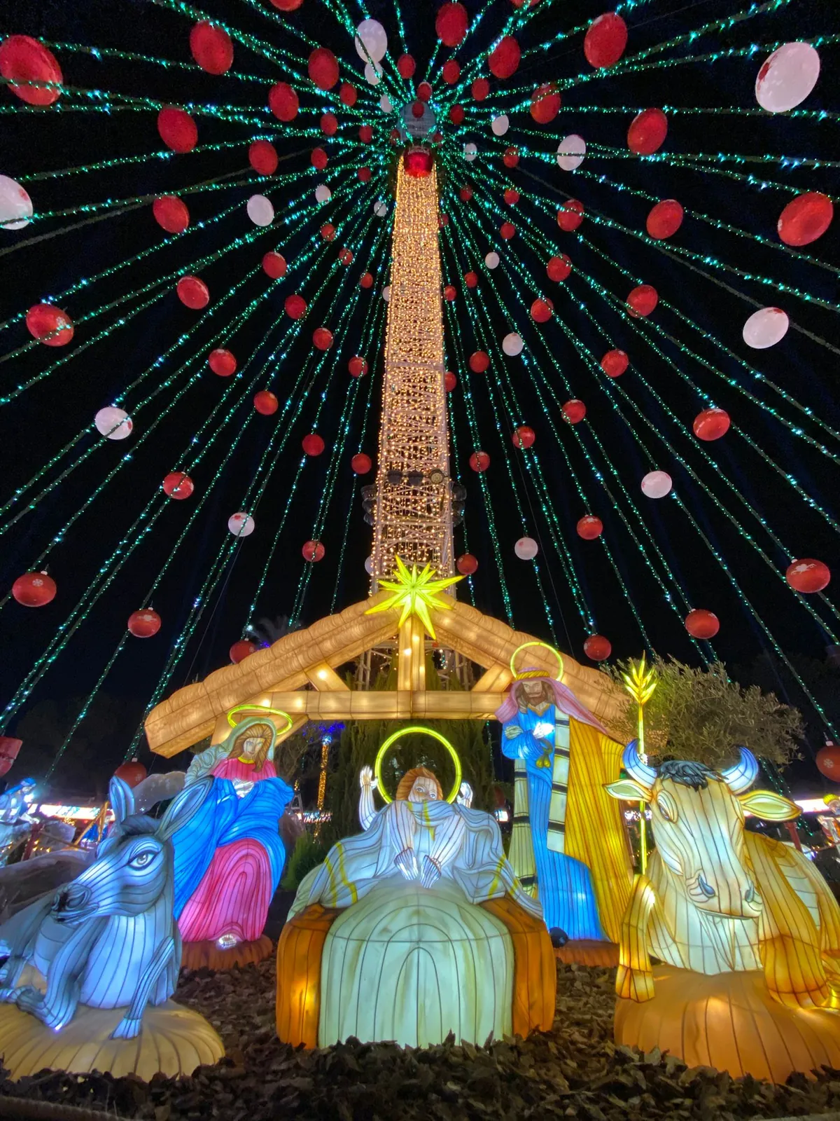 Portal de Belén luminoso bajo un abanico de luces con bolas rojas y blancas
